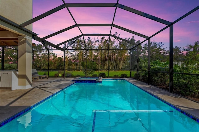 pool at dusk featuring glass enclosure, a patio, and a pool with connected hot tub