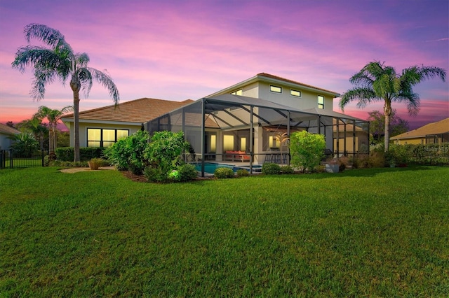 back house at dusk with a lawn and glass enclosure