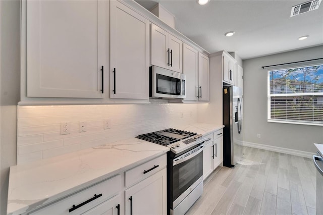 kitchen with light stone countertops, appliances with stainless steel finishes, decorative backsplash, light hardwood / wood-style flooring, and white cabinetry