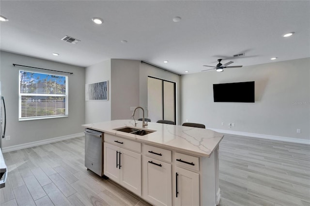 kitchen with light stone counters, a kitchen island with sink, sink, dishwasher, and white cabinetry