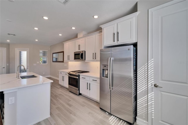 kitchen with a center island with sink, sink, light stone countertops, appliances with stainless steel finishes, and white cabinetry