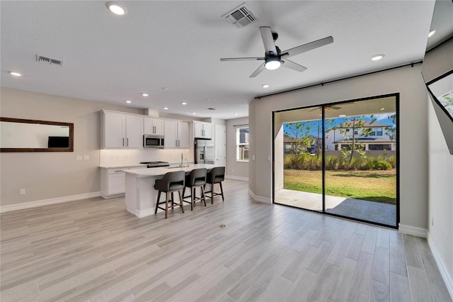 kitchen with appliances with stainless steel finishes, light wood-type flooring, a kitchen breakfast bar, a kitchen island with sink, and white cabinets