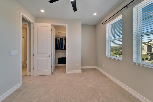 unfurnished bedroom featuring light carpet, a closet, a spacious closet, and ceiling fan