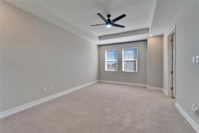 carpeted spare room with a raised ceiling and ceiling fan