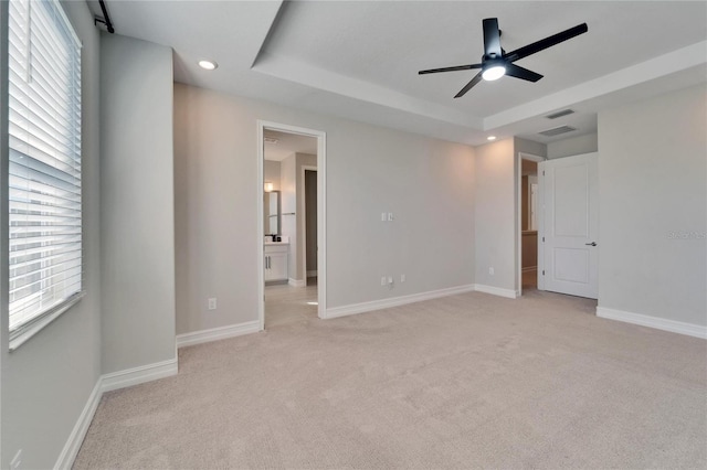 unfurnished bedroom featuring ceiling fan, a raised ceiling, light carpet, and ensuite bath