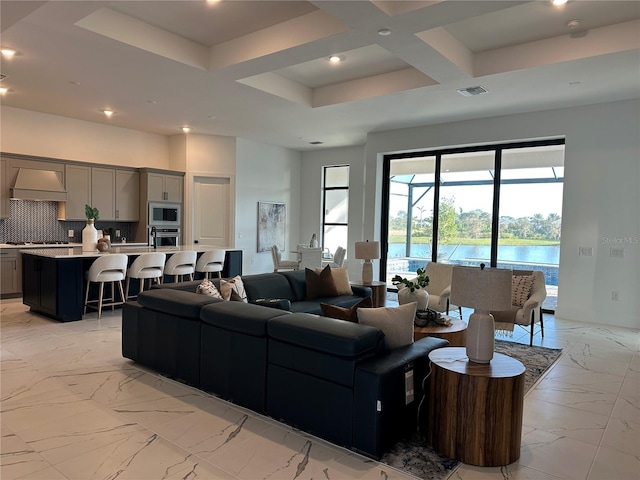 living room with a water view, beam ceiling, and coffered ceiling