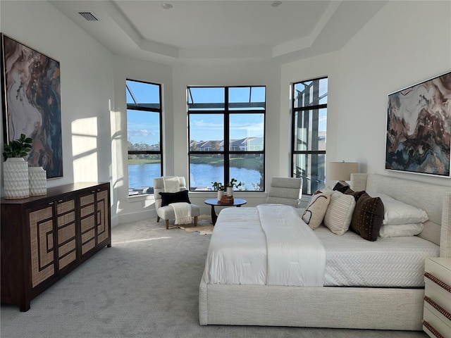 carpeted bedroom with a water view and a tray ceiling