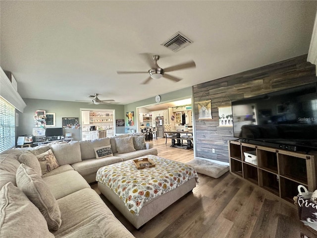 living area featuring visible vents, wood finished floors, ceiling fan, and wooden walls