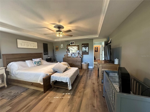bedroom with wood finished floors, ceiling fan, ornamental molding, and a tray ceiling