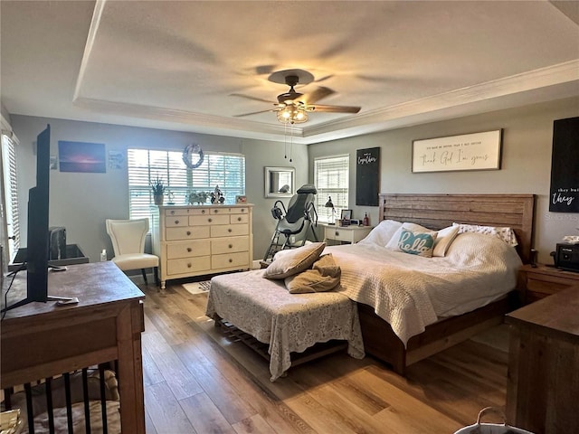 bedroom with hardwood / wood-style floors, a raised ceiling, ceiling fan, and crown molding