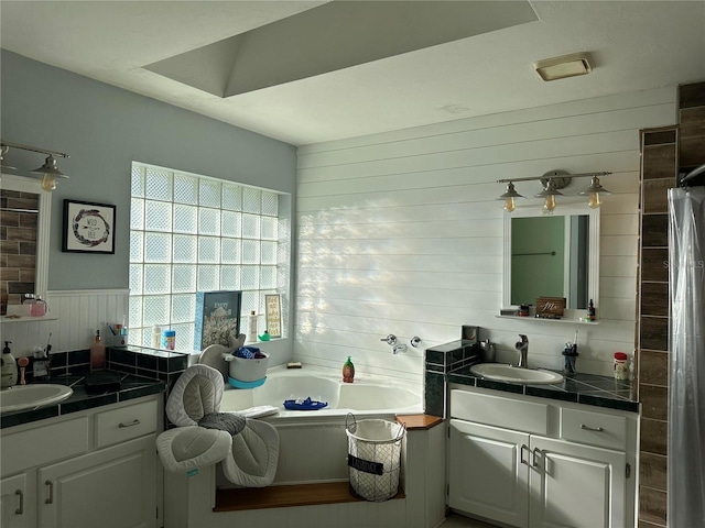 bathroom with two vanities, a bath, wainscoting, and a sink