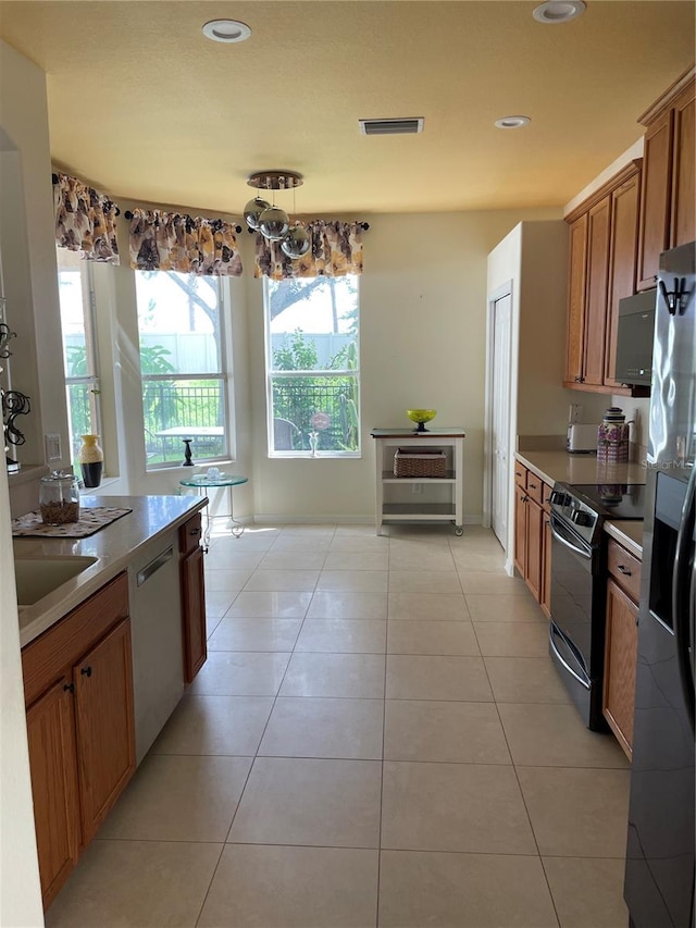 kitchen featuring sink, appliances with stainless steel finishes, light tile patterned flooring, and decorative light fixtures