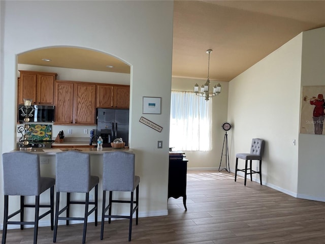 kitchen featuring black fridge, a breakfast bar, a chandelier, dark hardwood / wood-style floors, and pendant lighting