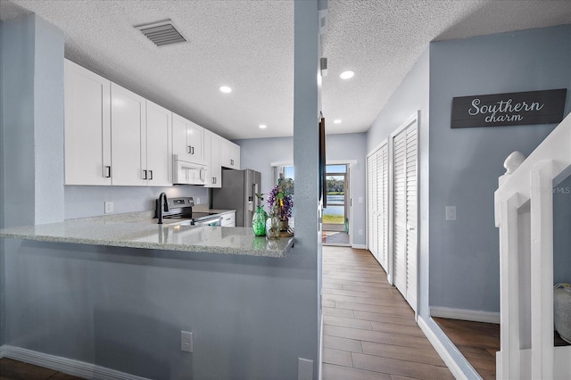 kitchen with light stone countertops, appliances with stainless steel finishes, dark hardwood / wood-style flooring, kitchen peninsula, and white cabinets