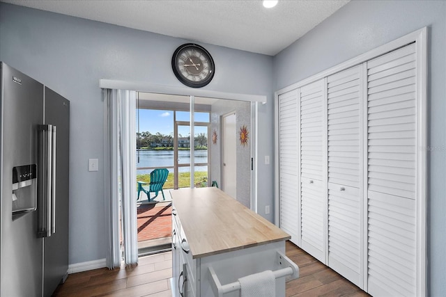 interior space featuring butcher block counters, dark wood-type flooring, stainless steel fridge with ice dispenser, a textured ceiling, and a water view