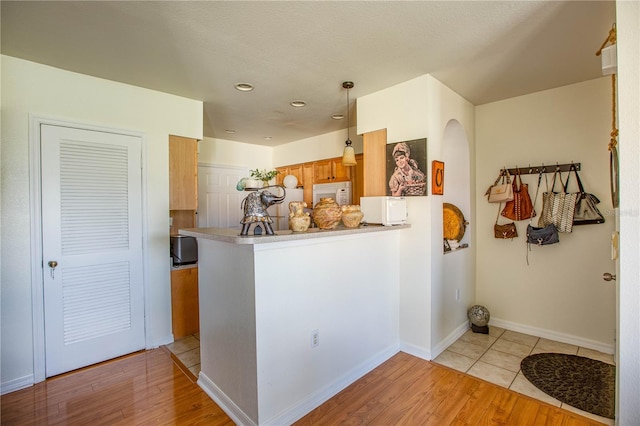 kitchen with hanging light fixtures, light hardwood / wood-style flooring, kitchen peninsula, and a textured ceiling