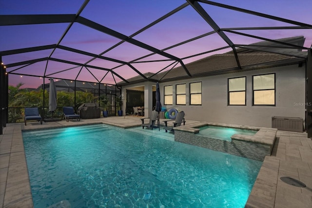 pool at dusk featuring glass enclosure, an in ground hot tub, and a patio area