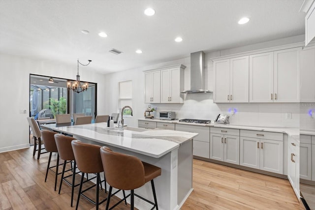 kitchen featuring light hardwood / wood-style floors, wall chimney exhaust hood, and a center island with sink