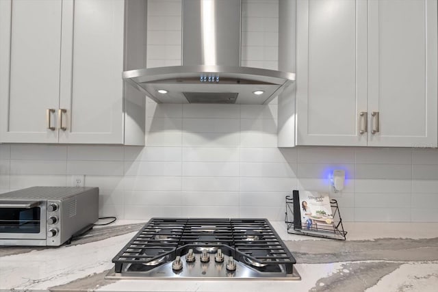 kitchen with stainless steel gas cooktop, white cabinetry, range hood, and light stone counters