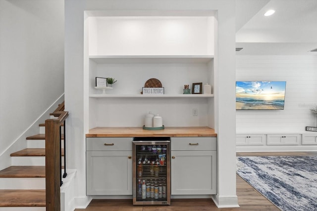 bar with wine cooler, wood-type flooring, gray cabinets, and wood counters