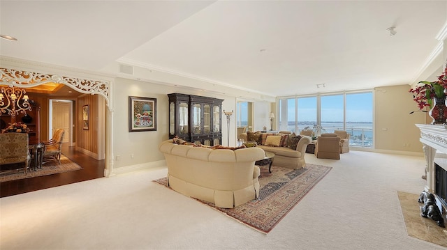 living room featuring crown molding, a wall of windows, light hardwood / wood-style floors, a water view, and a high end fireplace