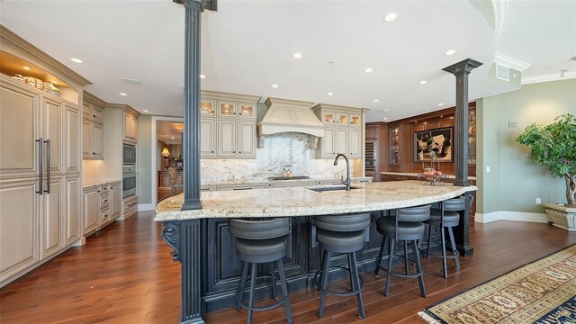 kitchen featuring ornamental molding, ornate columns, tasteful backsplash, and a large island with sink