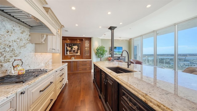 kitchen featuring dark hardwood / wood-style flooring, stainless steel gas stovetop, sink, backsplash, and light stone countertops