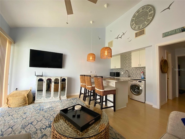 living room with washer / dryer, light wood-type flooring, ceiling fan, and lofted ceiling