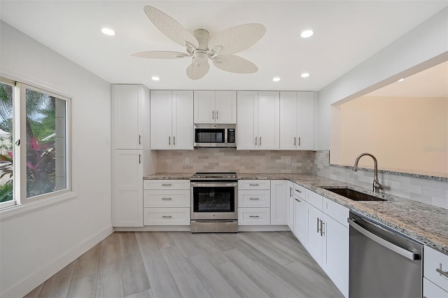 kitchen featuring appliances with stainless steel finishes, a sink, light stone counters, tasteful backsplash, and recessed lighting