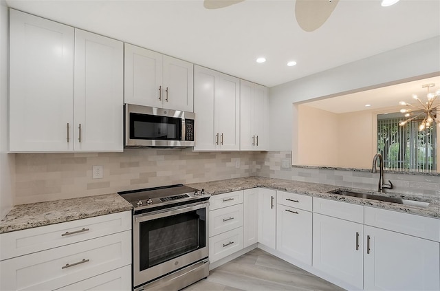 kitchen with appliances with stainless steel finishes, sink, backsplash, white cabinets, and a notable chandelier