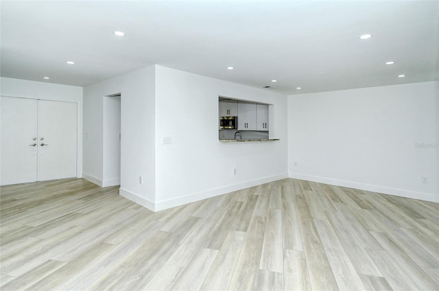 unfurnished living room featuring recessed lighting, light wood-style flooring, baseboards, and a sink