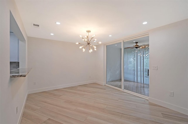 empty room with ceiling fan with notable chandelier and light hardwood / wood-style floors