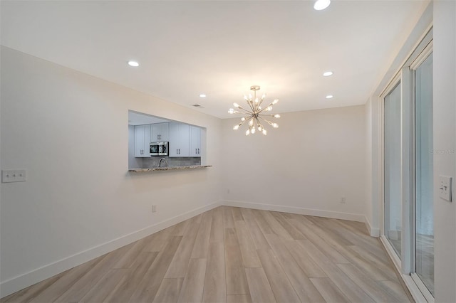 unfurnished dining area featuring a chandelier, light wood-style floors, recessed lighting, baseboards, and a sink