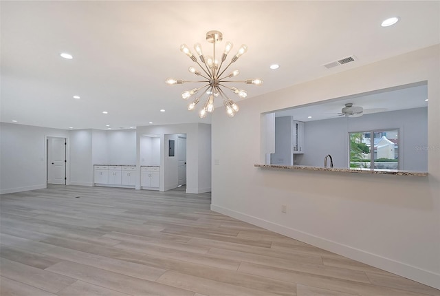 unfurnished living room with sink, ceiling fan with notable chandelier, and light hardwood / wood-style floors