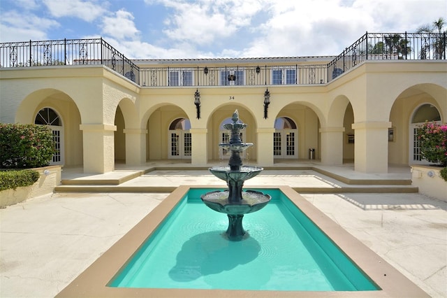 rear view of property featuring french doors, a balcony, a patio, and stucco siding