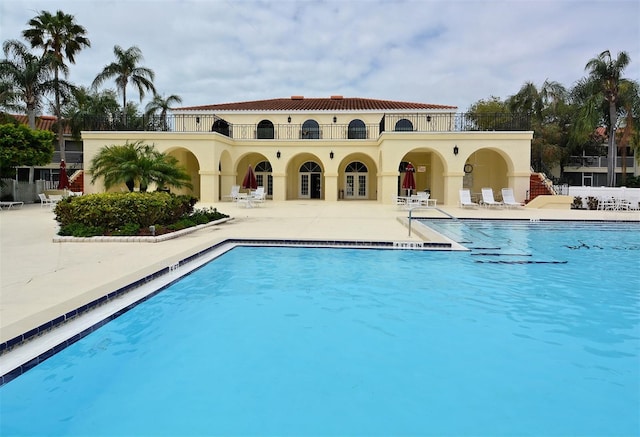 rear view of house featuring a patio area, a community pool, stucco siding, and a balcony