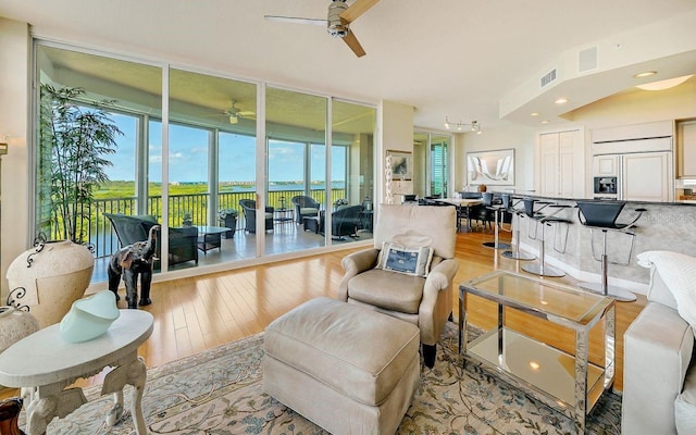 living room featuring ceiling fan, light hardwood / wood-style flooring, and a wall of windows