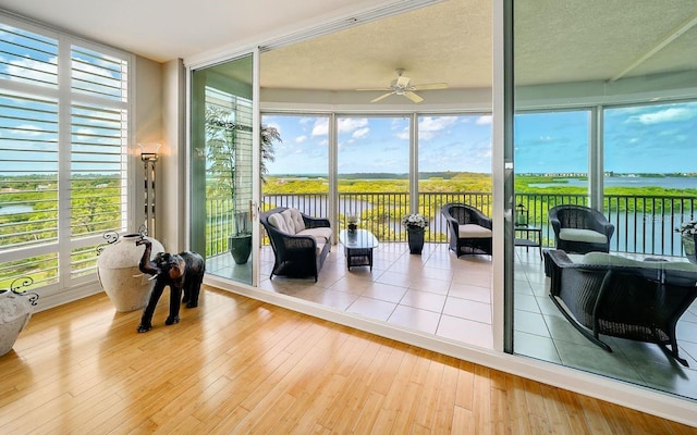 sunroom featuring a water view, wood-type flooring, and ceiling fan