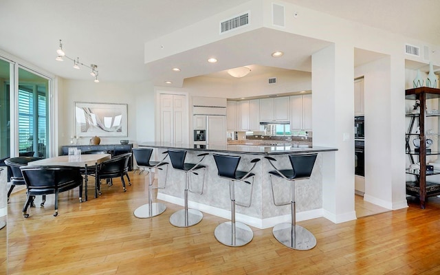 kitchen featuring a breakfast bar area, dark countertops, paneled built in refrigerator, and light wood-style flooring