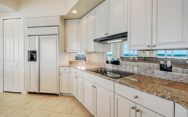 kitchen with black electric stovetop, paneled refrigerator, light stone countertops, light tile patterned floors, and white cabinets