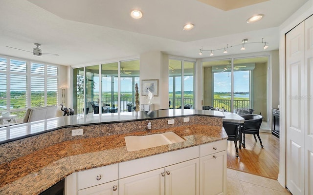 kitchen with a ceiling fan, white cabinets, light stone counters, a sink, and light tile patterned floors