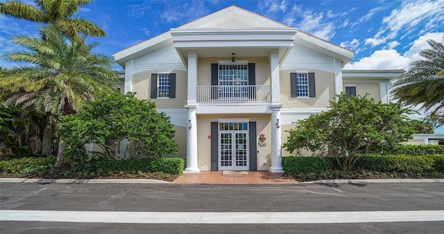 neoclassical home with french doors, stucco siding, and a balcony