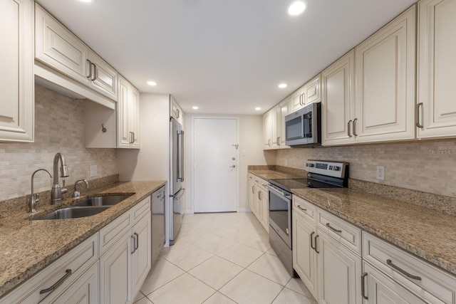 kitchen with stainless steel appliances, sink, light tile patterned floors, light stone counters, and tasteful backsplash