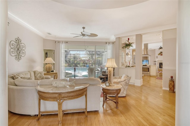 living room with light hardwood / wood-style floors, ornamental molding, and ceiling fan