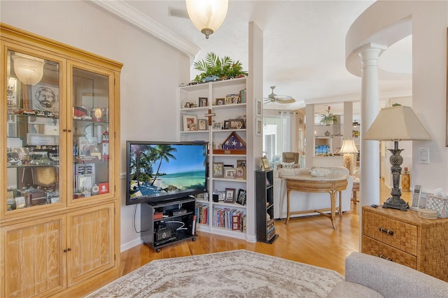 interior space with crown molding, decorative columns, light wood-type flooring, and ceiling fan