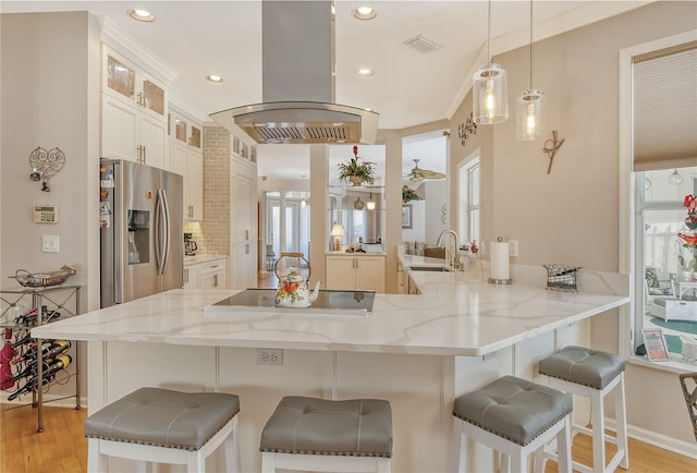 kitchen with kitchen peninsula, stainless steel refrigerator with ice dispenser, island range hood, and a breakfast bar area