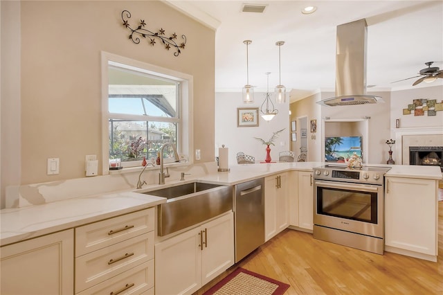 kitchen featuring appliances with stainless steel finishes, sink, island range hood, hanging light fixtures, and light hardwood / wood-style floors