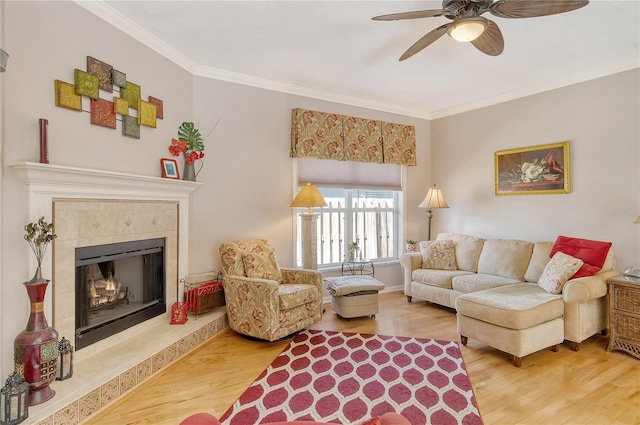 living room featuring ornamental molding, wood-type flooring, a tile fireplace, and ceiling fan