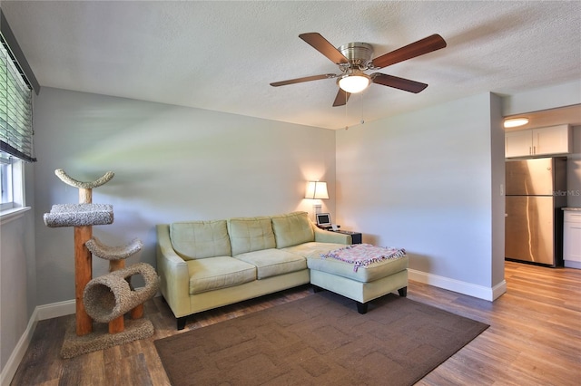 living room with a textured ceiling, light wood-type flooring, and ceiling fan