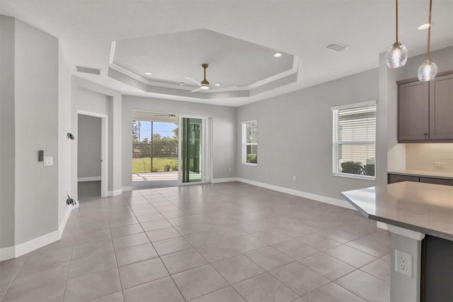 unfurnished living room featuring ceiling fan, a tray ceiling, and light tile patterned floors